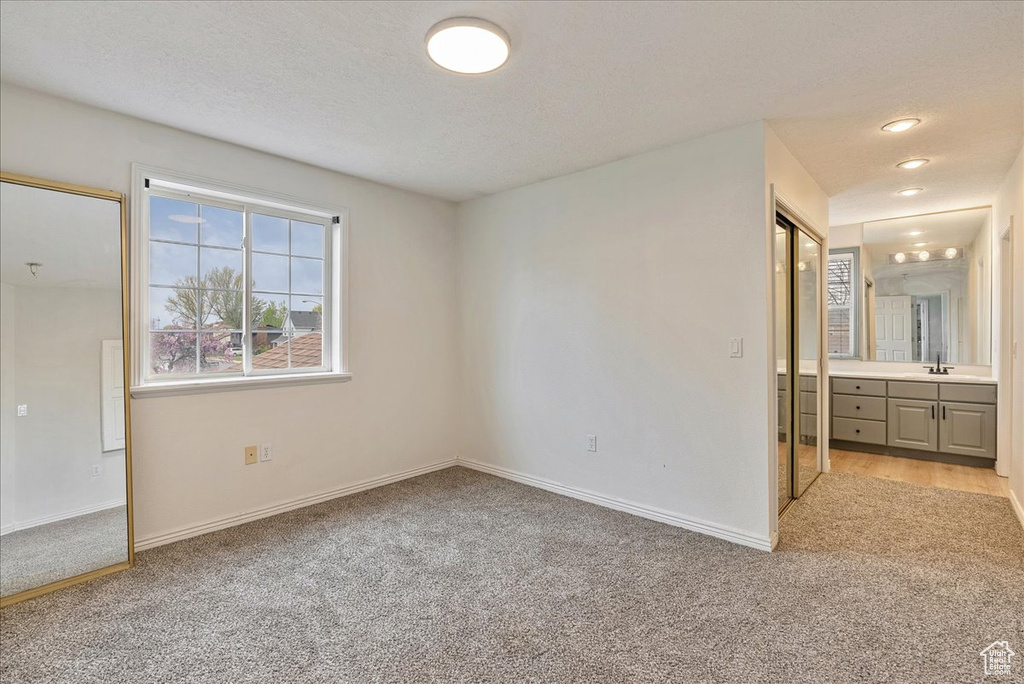 Unfurnished bedroom with light colored carpet, a sink, baseboards, and ensuite bathroom