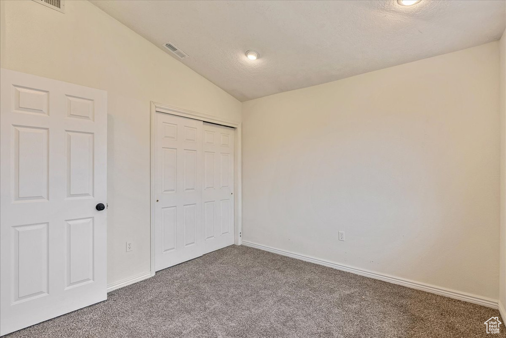 Unfurnished bedroom featuring visible vents, a closet, baseboards, carpet, and vaulted ceiling