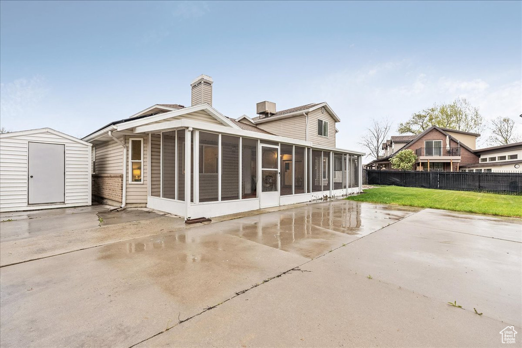 Rear view of property with fence, a storage unit, a sunroom, a lawn, and an outdoor structure