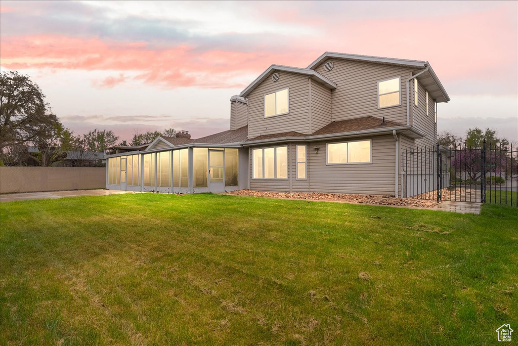 Back of property with a sunroom, a lawn, and fence