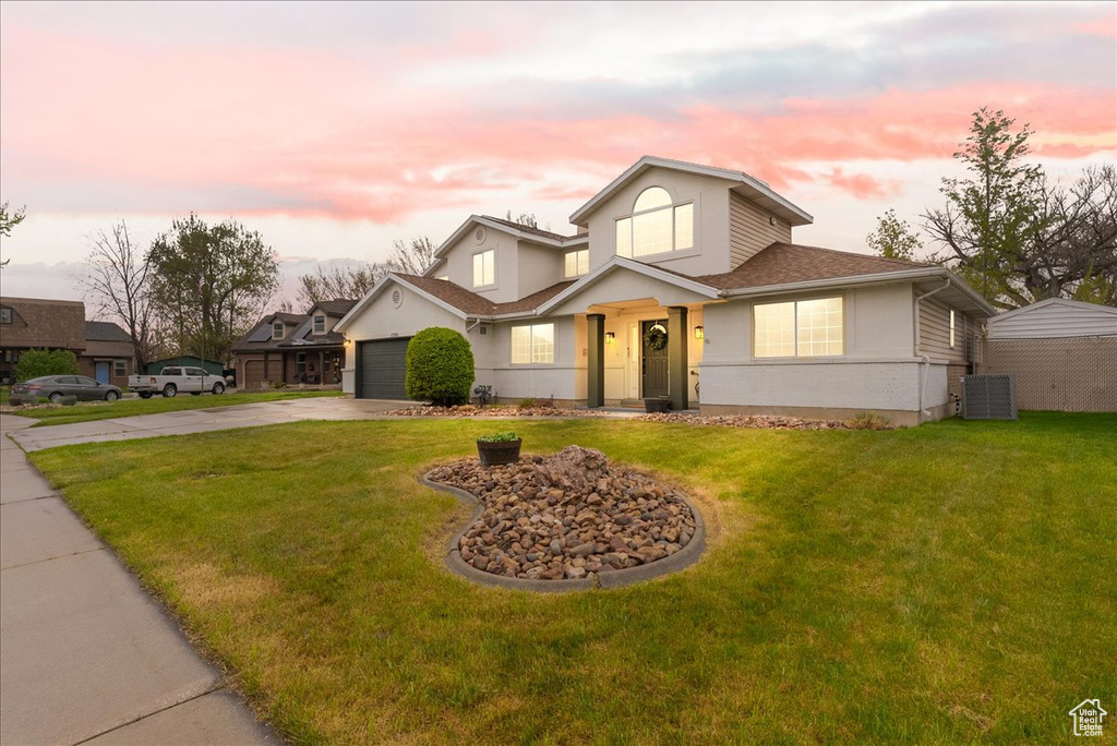 Traditional home with a garage, driveway, a front lawn, and stucco siding
