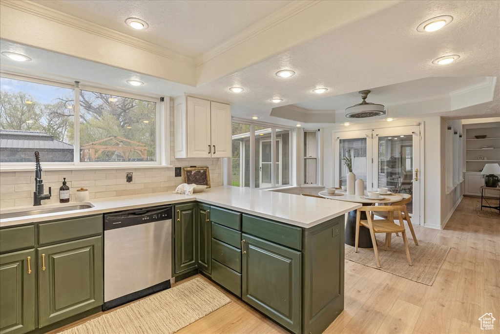 Kitchen with green cabinetry, a sink, a peninsula, stainless steel dishwasher, and a tray ceiling