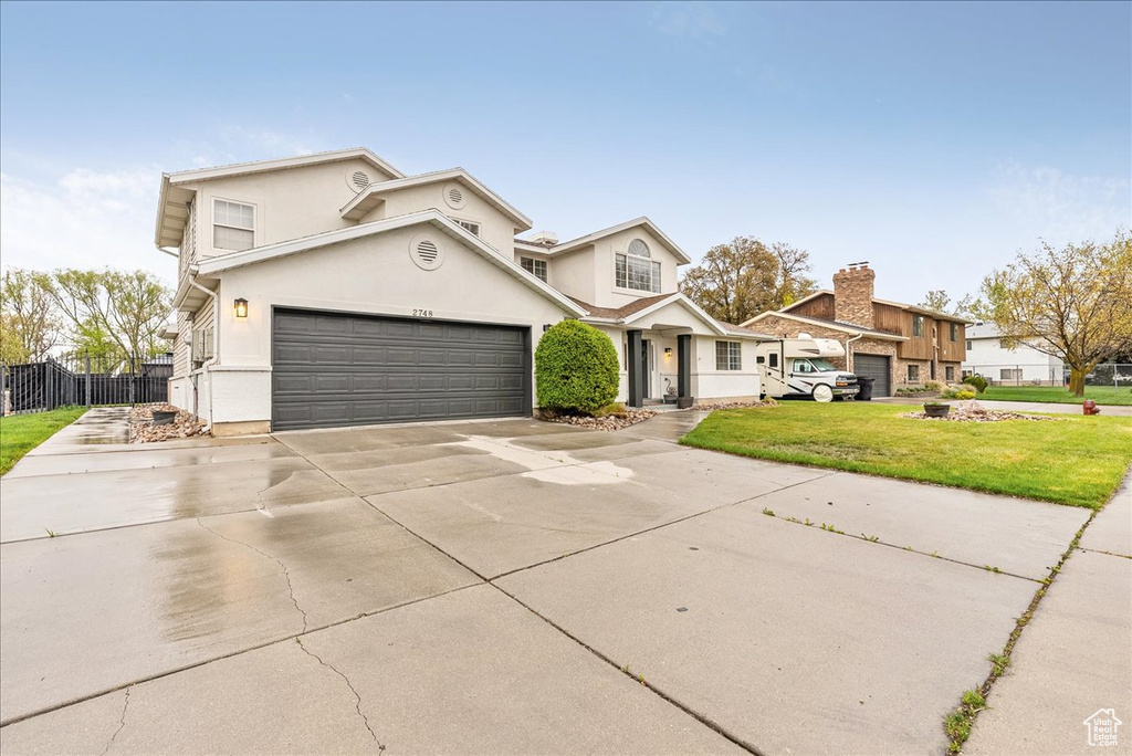 Traditional-style house with a front lawn, fence, stucco siding, concrete driveway, and an attached garage