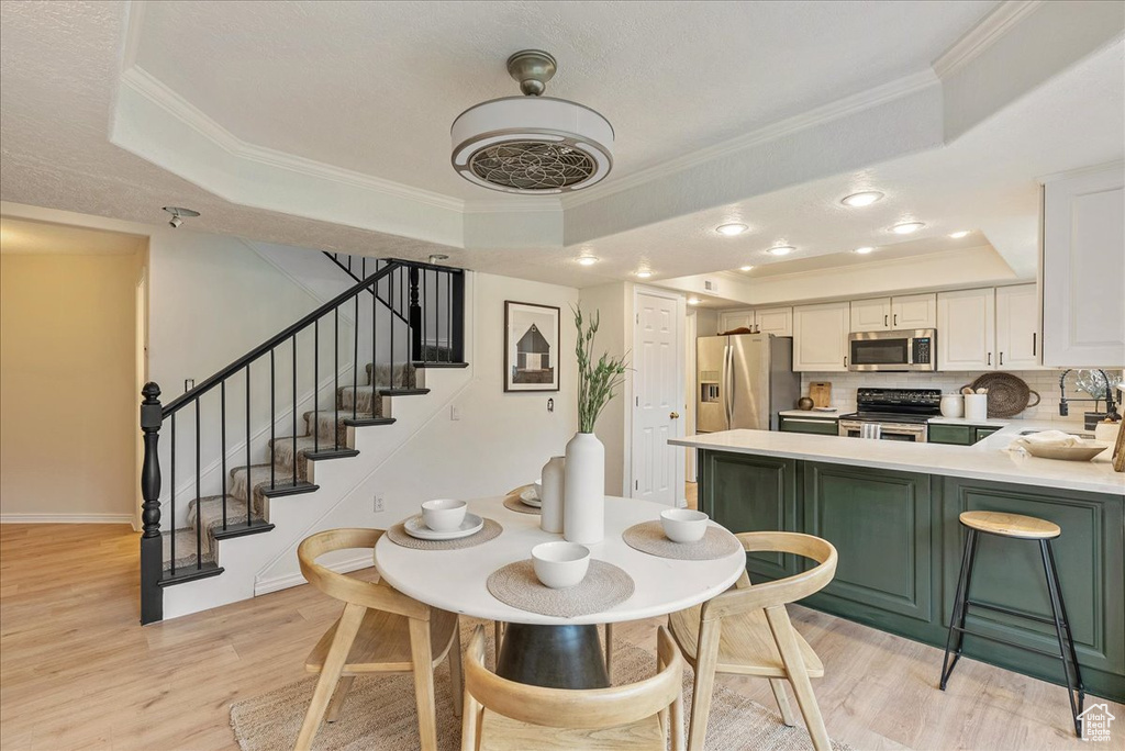 Dining room featuring ornamental molding, a raised ceiling, light wood finished floors, and stairs