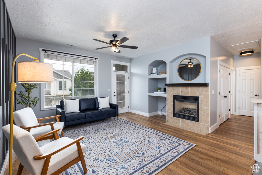 Living room with built in features, wood finished floors, baseboards, ceiling fan, and a textured ceiling