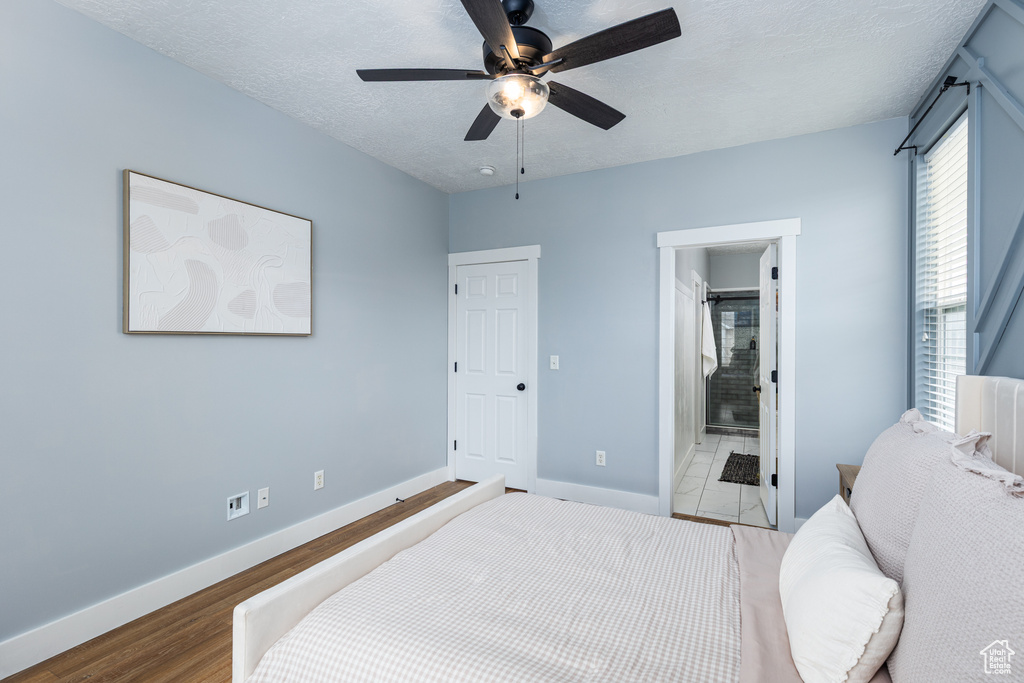 Bedroom with ceiling fan, a textured ceiling, wood finished floors, baseboards, and connected bathroom