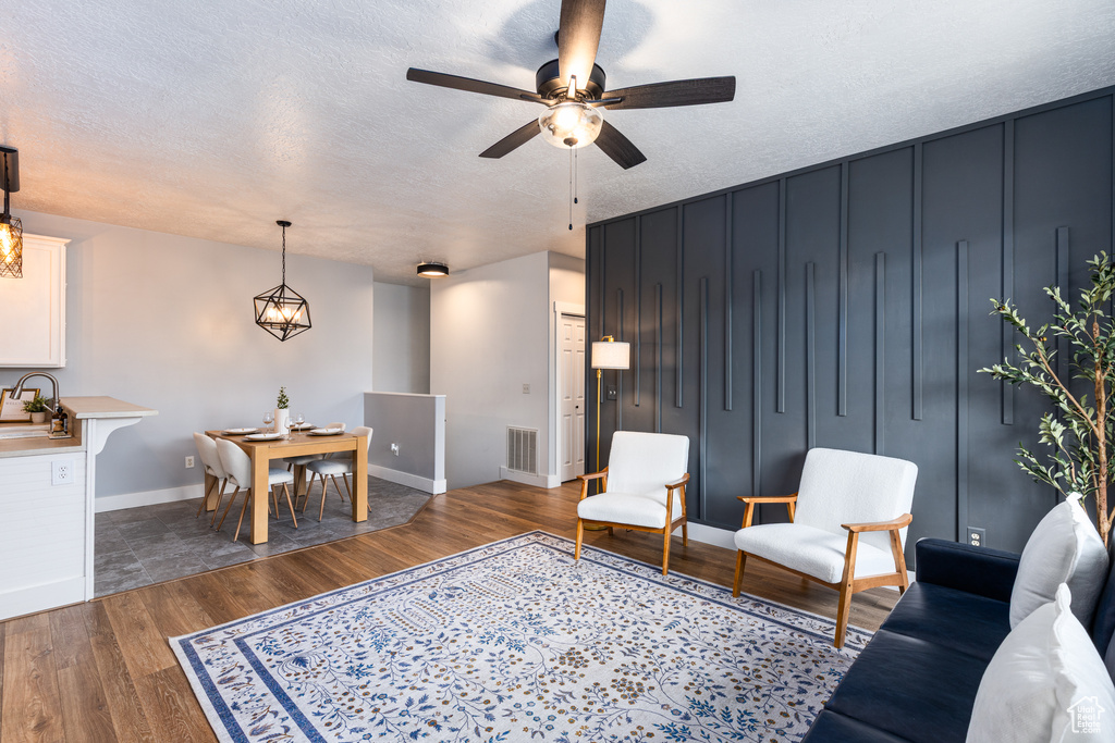 Living area with visible vents, baseboards, dark wood-style floors, a textured ceiling, and a ceiling fan