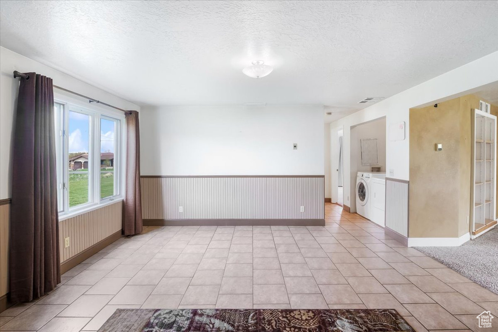 Spare room with light tile patterned flooring, a textured ceiling, a wainscoted wall, baseboards, and washer and clothes dryer