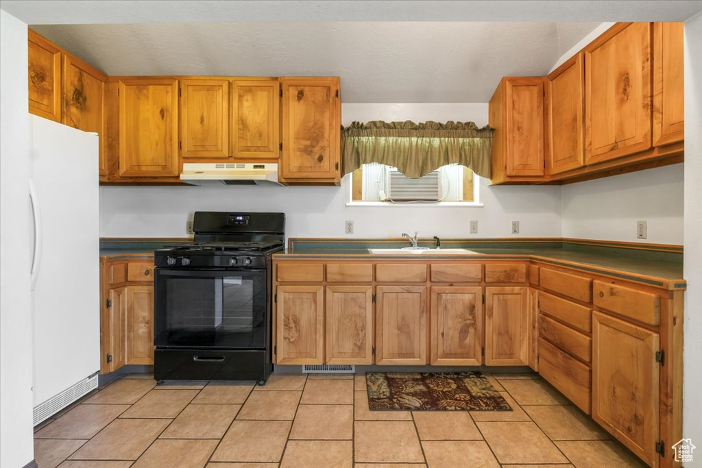 Kitchen with dark countertops, a sink, black range with gas stovetop, freestanding refrigerator, and under cabinet range hood