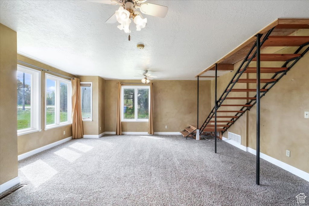 Unfurnished living room featuring stairway, ceiling fan, baseboards, and carpet