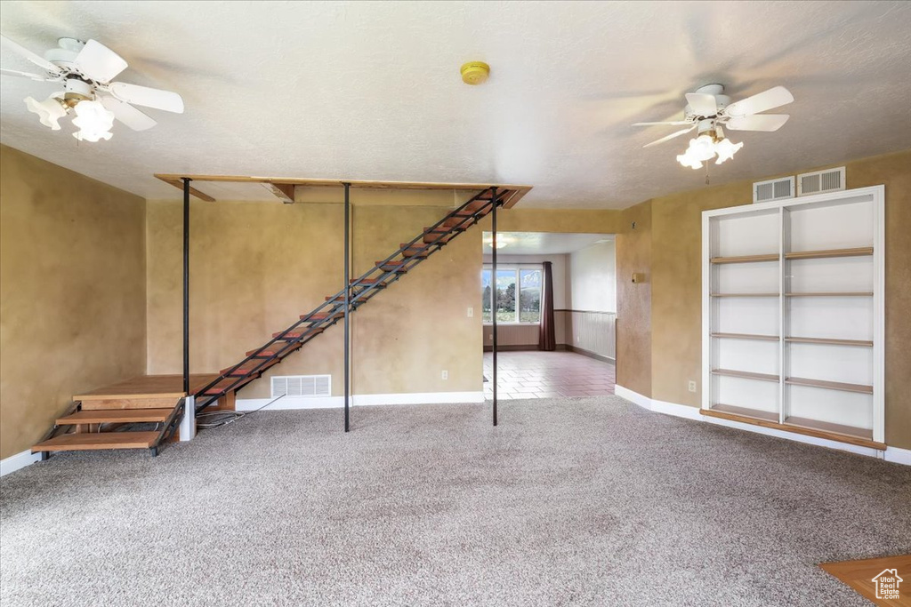 Unfurnished living room featuring carpet floors, a ceiling fan, and visible vents