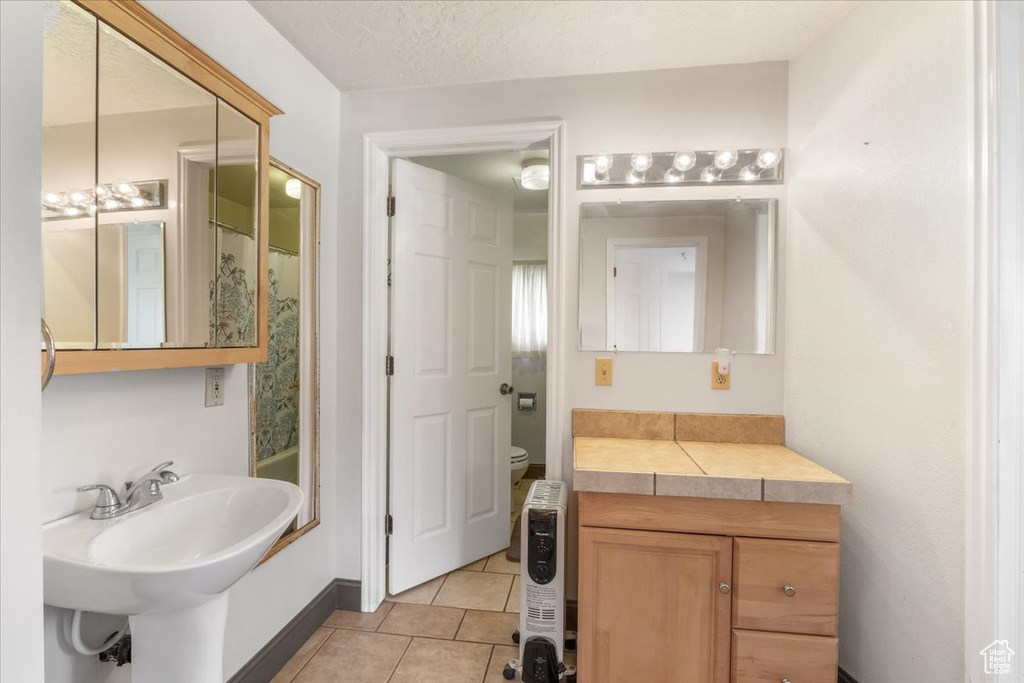 Bathroom featuring a sink, toilet, tile patterned floors, baseboards, and a shower with curtain