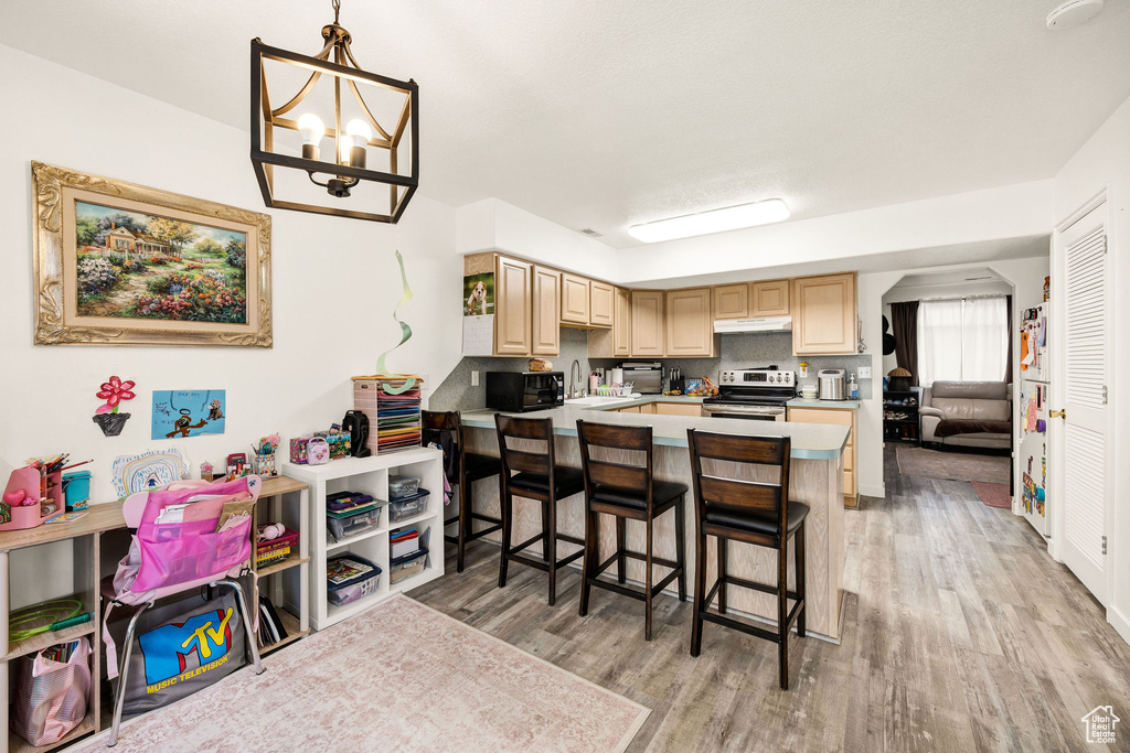Kitchen featuring a kitchen breakfast bar, stainless steel range with electric cooktop, light brown cabinets, under cabinet range hood, and light wood-style flooring