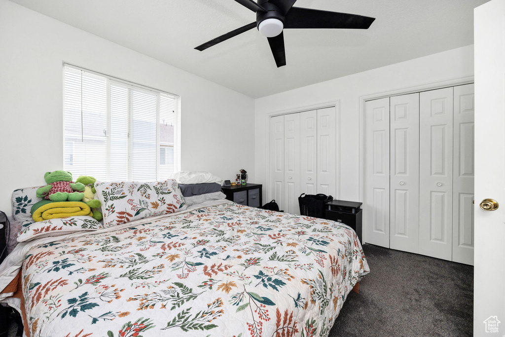 Bedroom with ceiling fan, multiple closets, and dark carpet