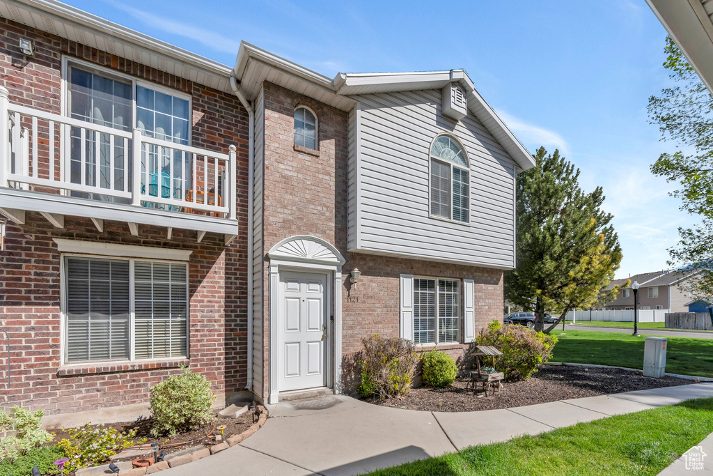 View of property featuring brick siding, a balcony, and a front yard