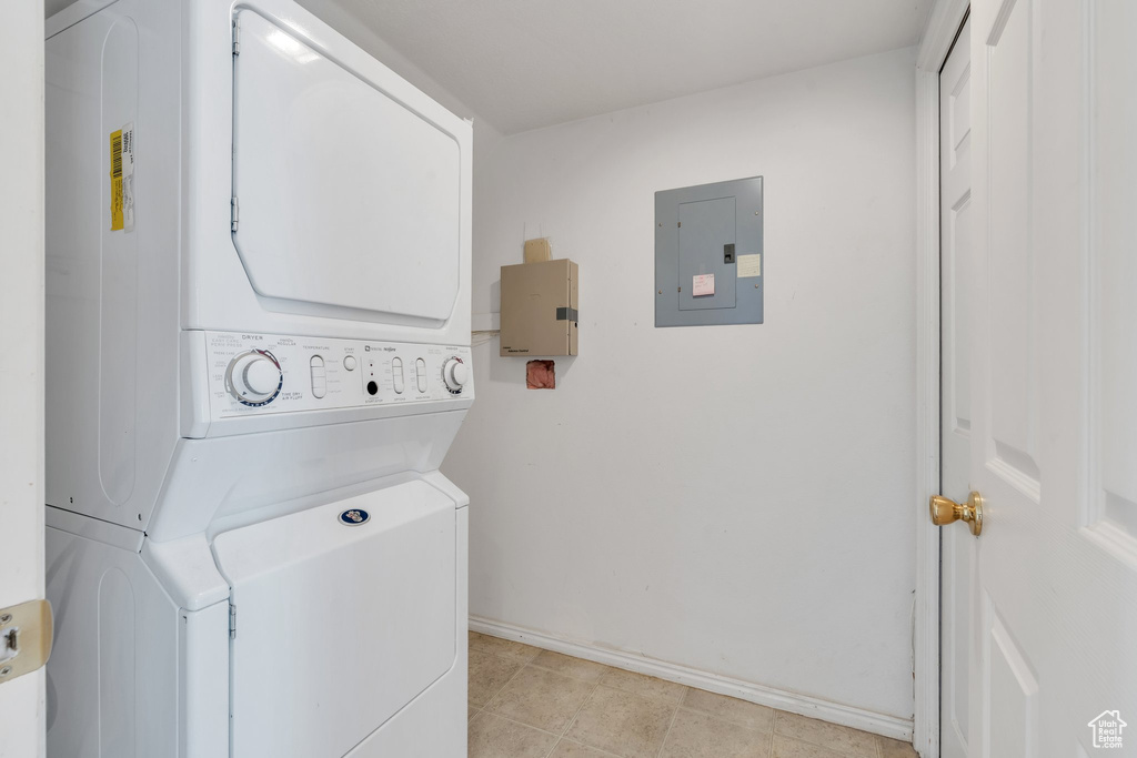 Clothes washing area featuring baseboards, electric panel, stacked washer / dryer, and laundry area