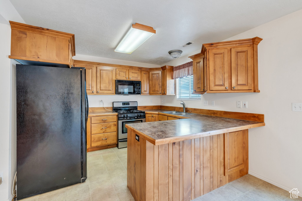 Kitchen featuring brown cabinets, a sink, a peninsula, visible vents, and black appliances