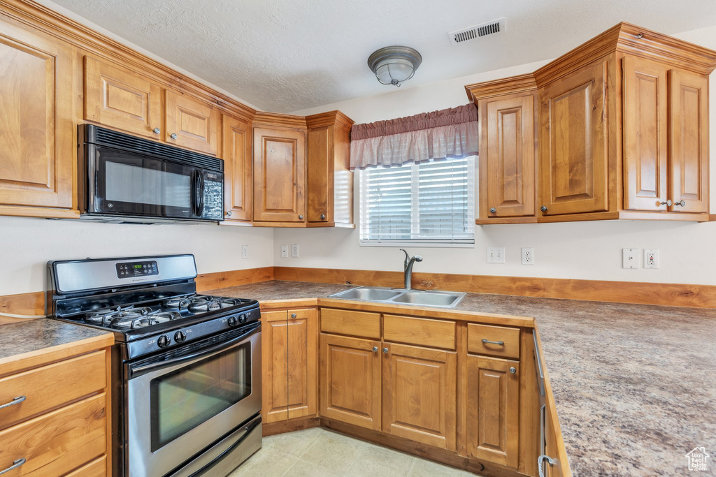Kitchen with visible vents, brown cabinetry, stainless steel gas stove, black microwave, and a sink