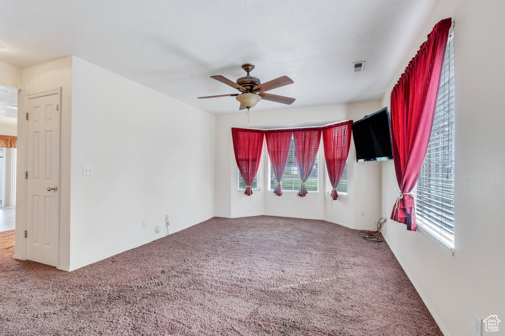 Carpeted empty room featuring baseboards, ceiling fan, and visible vents