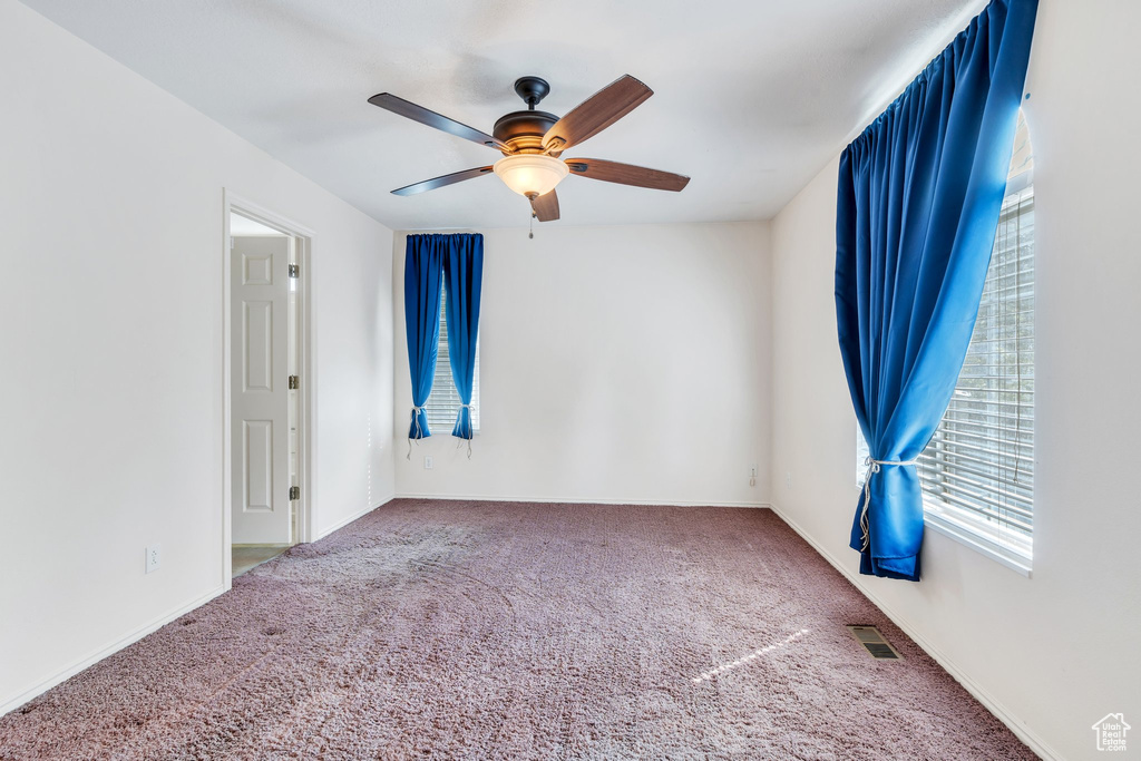 Carpeted empty room featuring ceiling fan, visible vents, and baseboards