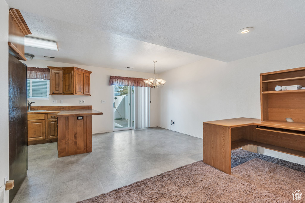 Kitchen with brown cabinets, a notable chandelier, a sink, a textured ceiling, and decorative light fixtures
