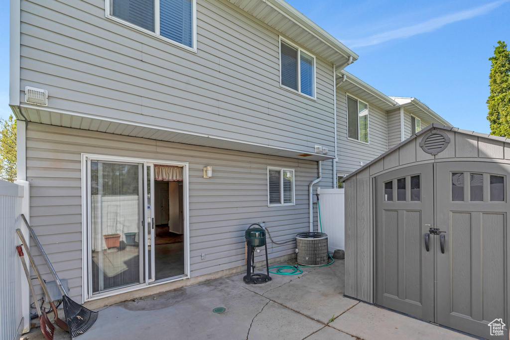 Rear view of property with a storage shed, an outbuilding, cooling unit, fence, and a patio