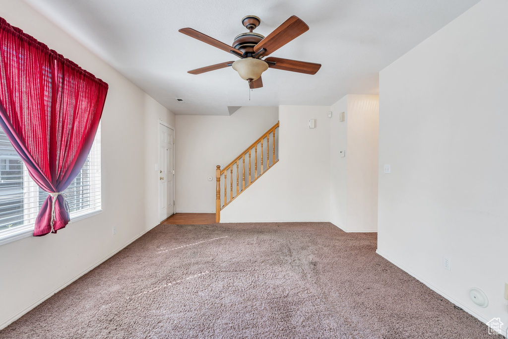 Unfurnished room with carpet floors, ceiling fan, and stairway