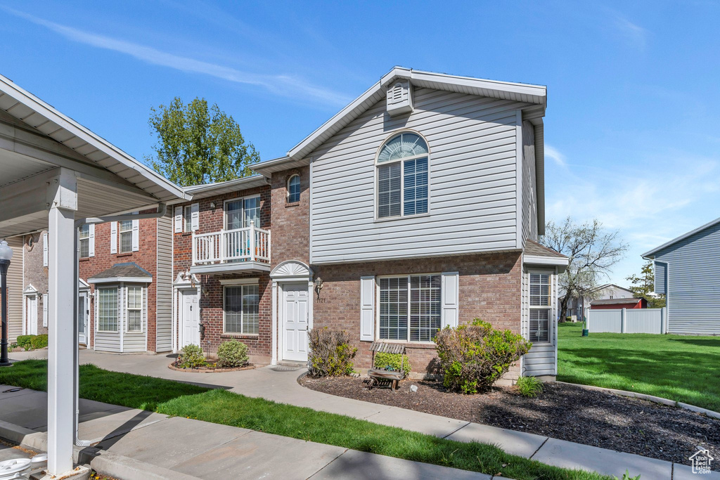 View of property with a balcony, a front yard, and brick siding