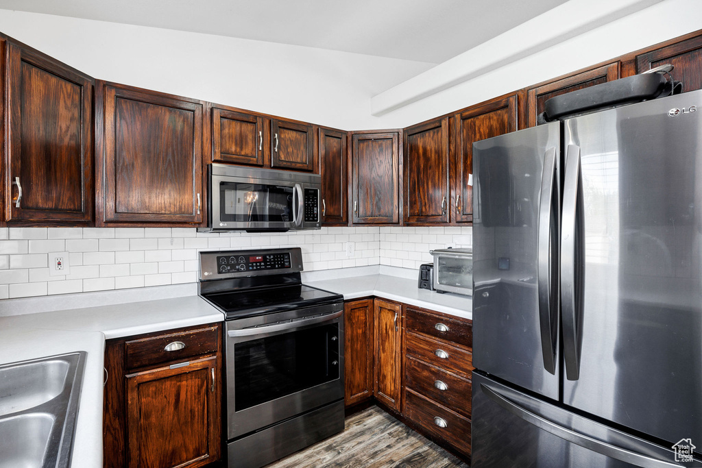 Kitchen with dark brown cabinets, appliances with stainless steel finishes, a sink, light countertops, and backsplash