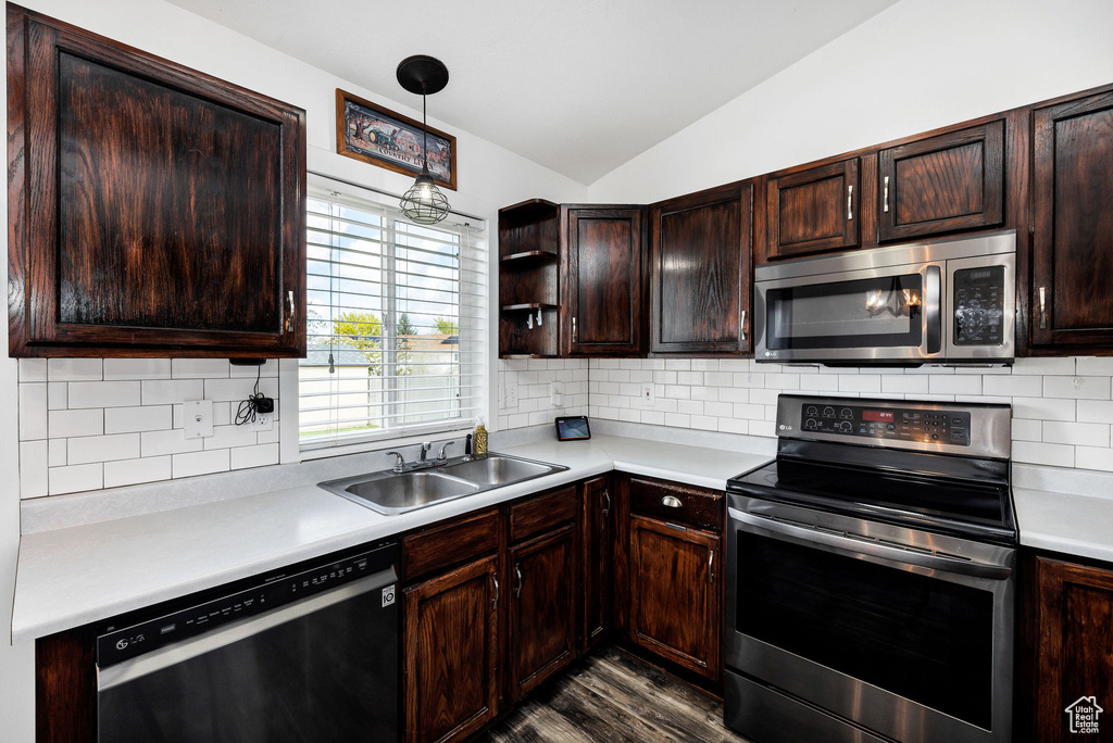 Kitchen with dark wood-style floors, light countertops, a sink, appliances with stainless steel finishes, and vaulted ceiling