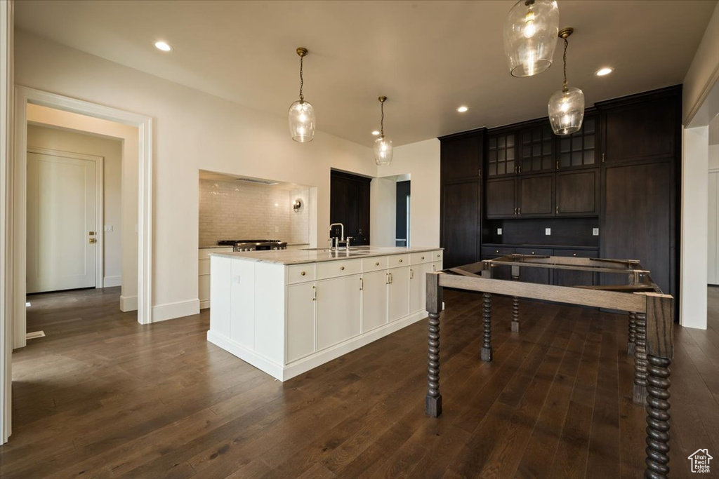 Kitchen featuring light countertops, a center island with sink, dark wood-style floors, and glass insert cabinets