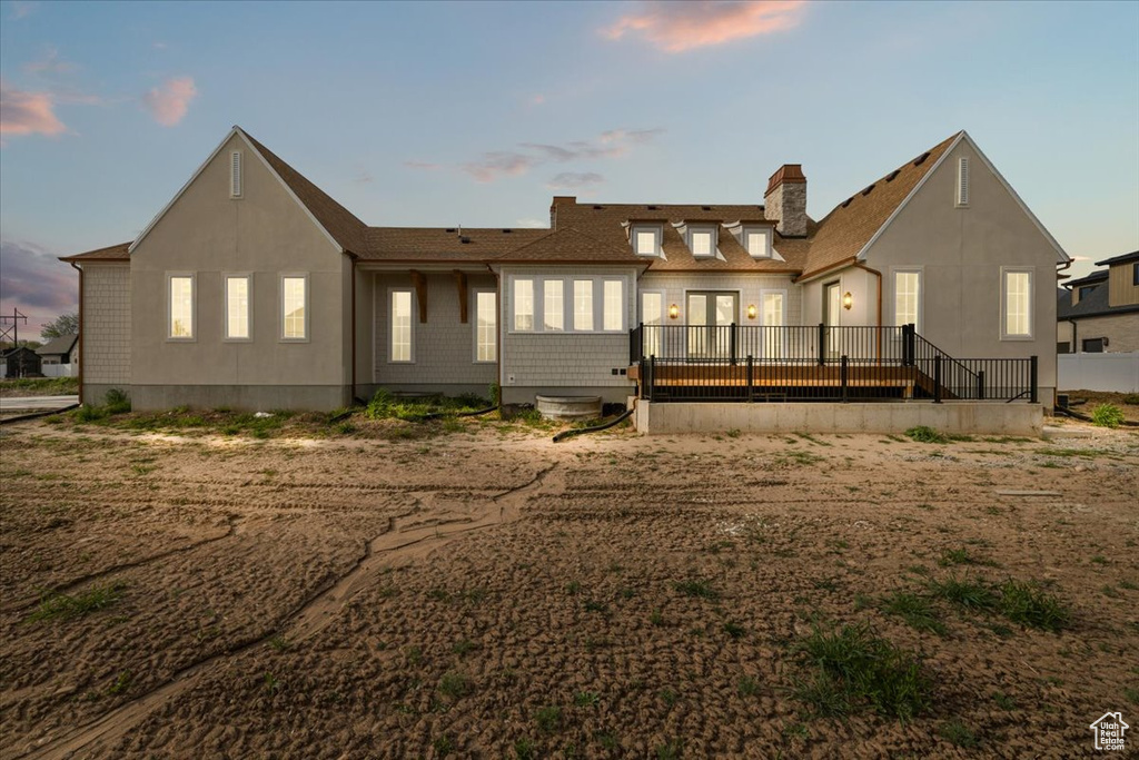 Back of property at dusk with a chimney and a deck