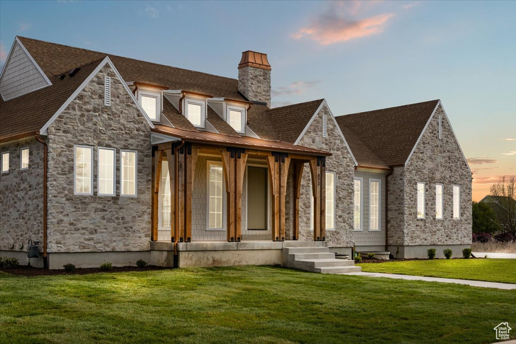 View of front of house with a chimney, a yard, a porch, and stone siding