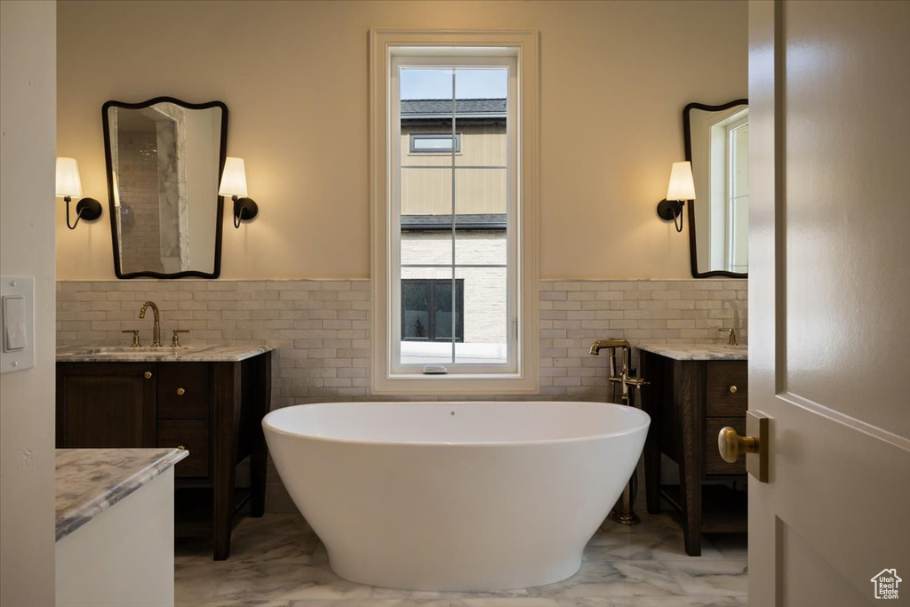 Full bathroom featuring tile walls, wainscoting, a sink, and marble finish floor
