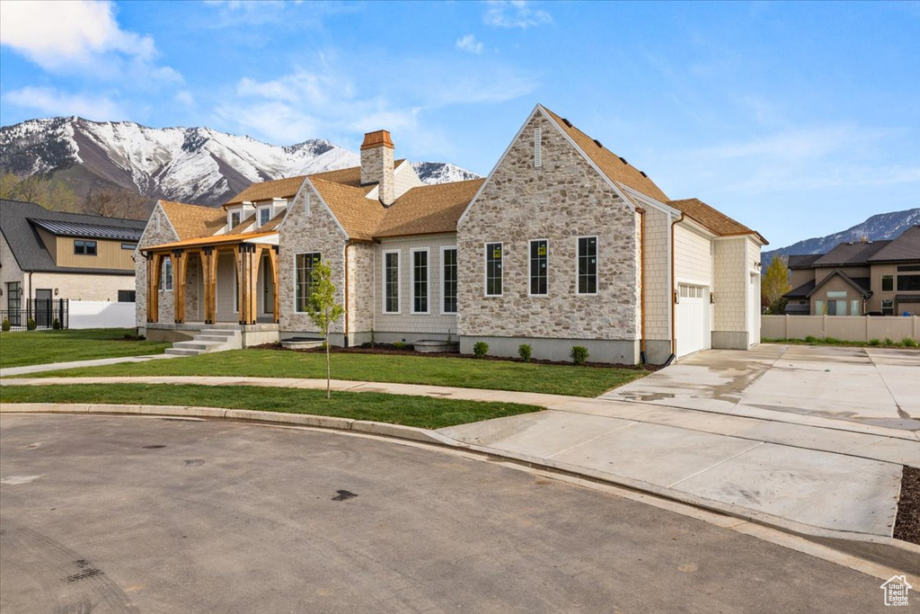 View of front facade featuring driveway, a chimney, fence, a mountain view, and stone siding
