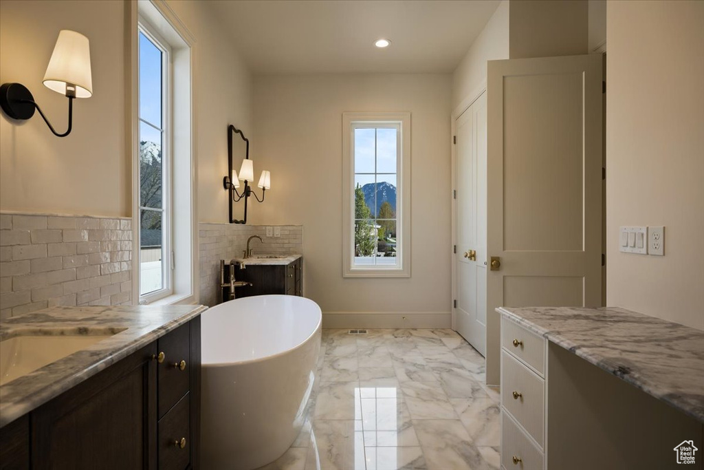 Full bath with vanity, marble finish floor, recessed lighting, backsplash, and a soaking tub