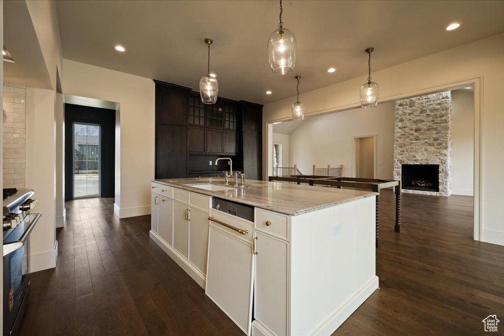 Kitchen with a kitchen island with sink, dark wood-style flooring, a sink, light stone counters, and range with gas stovetop