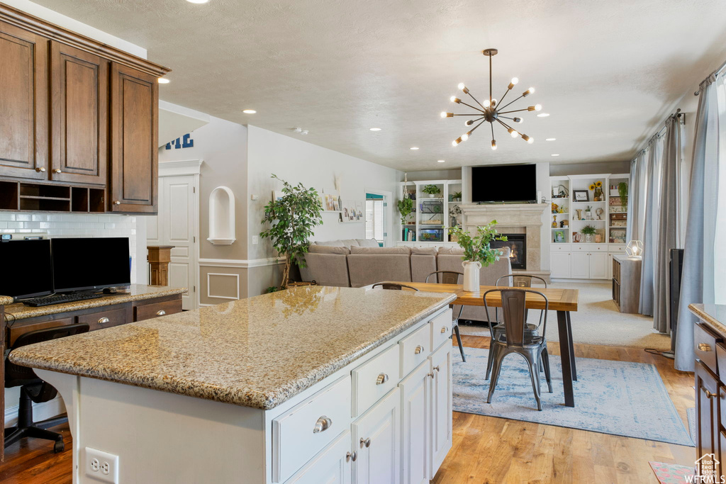 Kitchen with a fireplace, light stone countertops, open floor plan, a chandelier, and light wood finished floors