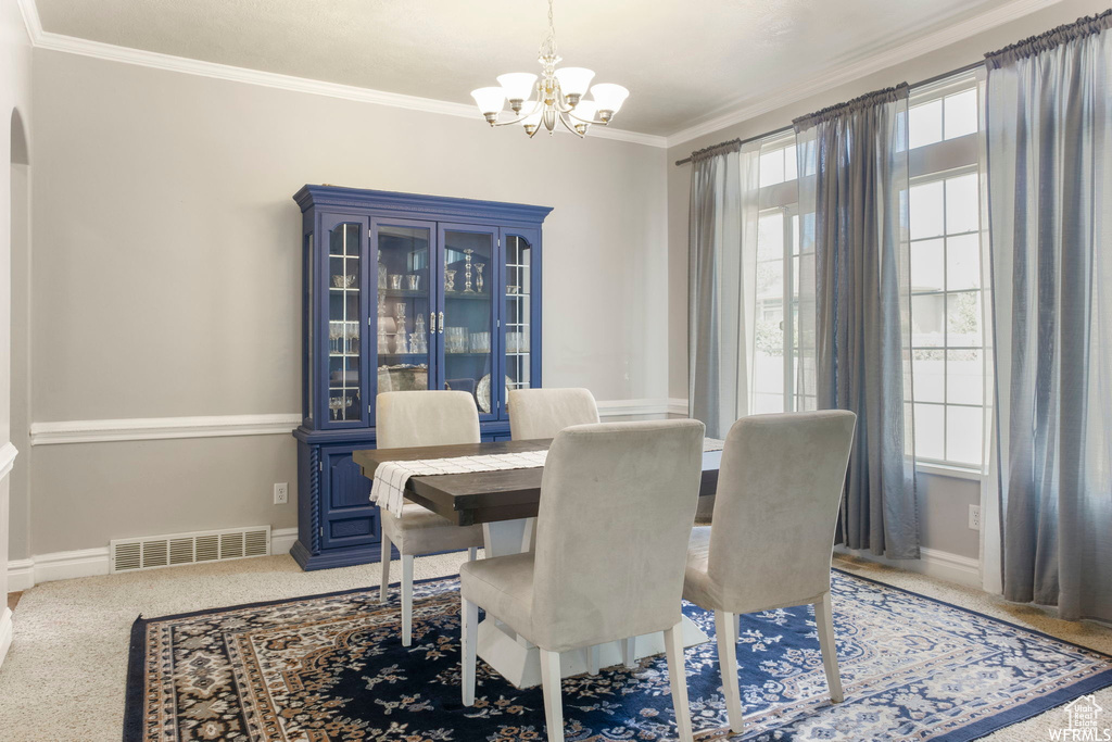 Carpeted dining space featuring visible vents, crown molding, arched walkways, baseboards, and a notable chandelier