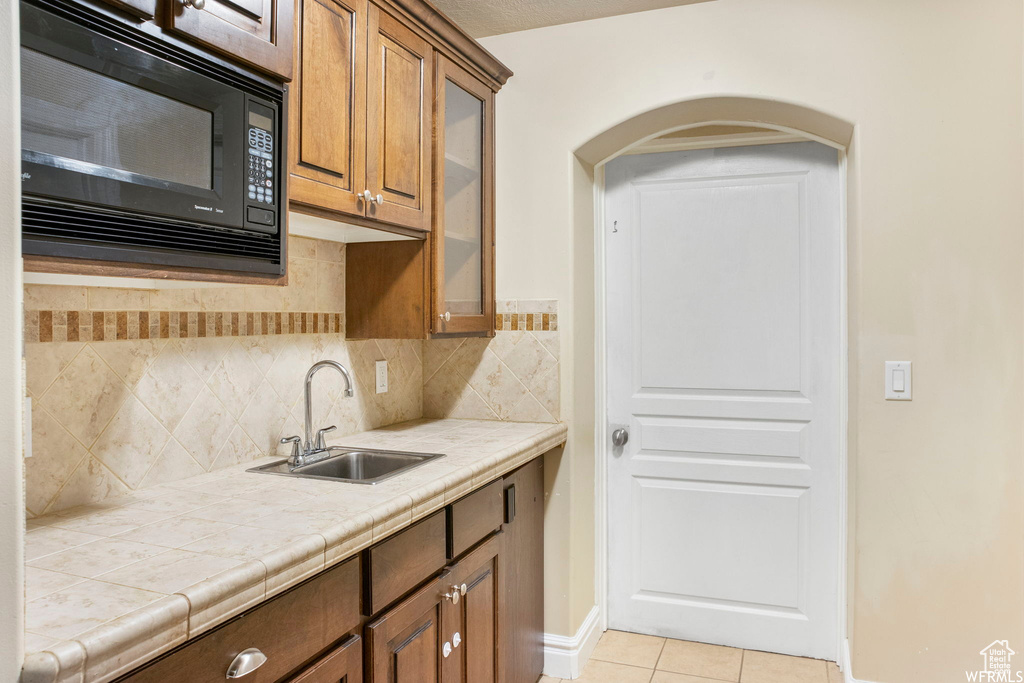 Kitchen with backsplash, black microwave, arched walkways, light tile patterned floors, and a sink