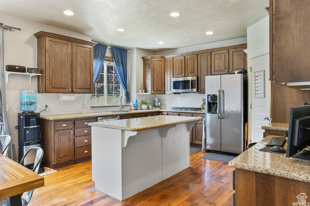 Kitchen with light stone counters, decorative backsplash, a center island, and stainless steel appliances