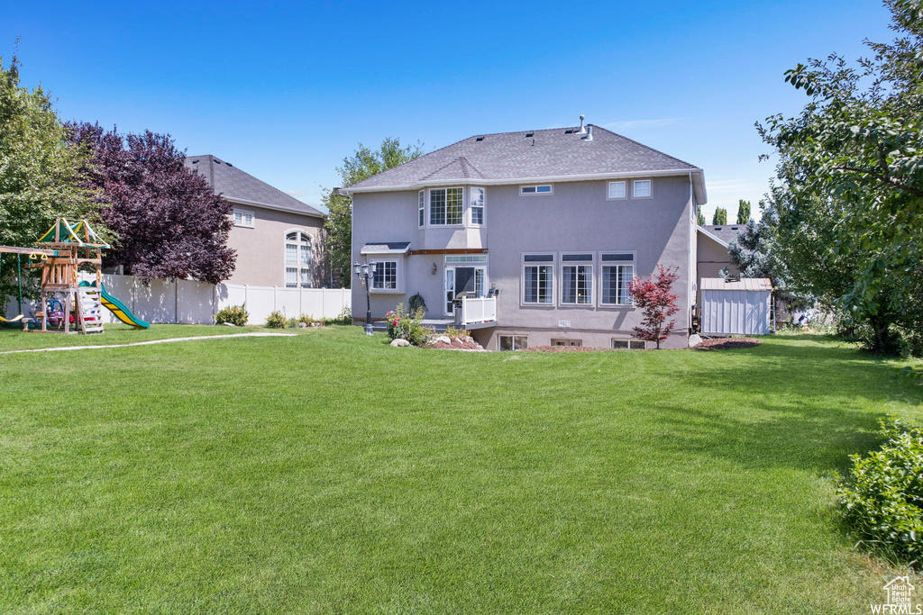 Rear view of property featuring a lawn, fence, a playground, and stucco siding