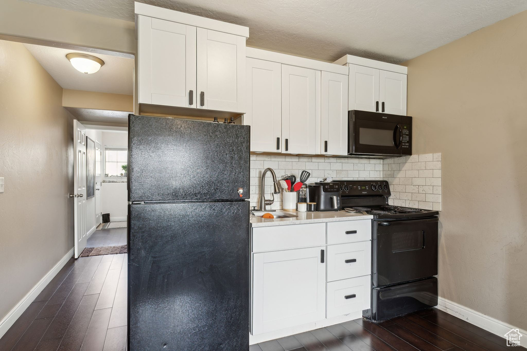 Kitchen featuring baseboards, dark wood-style floors, tasteful backsplash, a sink, and black appliances