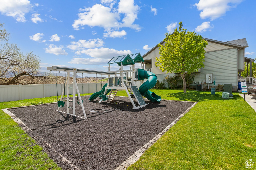 View of jungle gym with a yard, fence, and central air condition unit