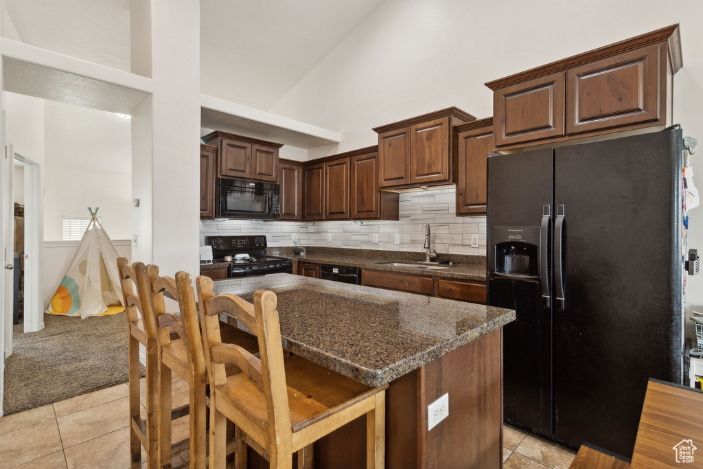 Kitchen with a sink, high vaulted ceiling, black appliances, and light tile patterned flooring