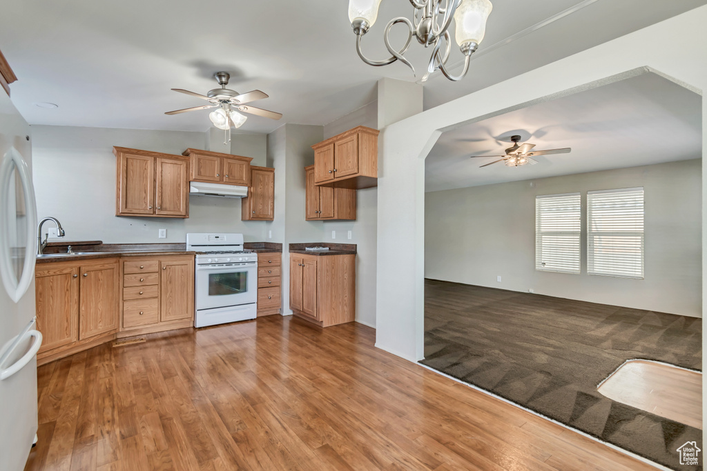 Kitchen featuring dark countertops, ceiling fan with notable chandelier, white appliances, and under cabinet range hood