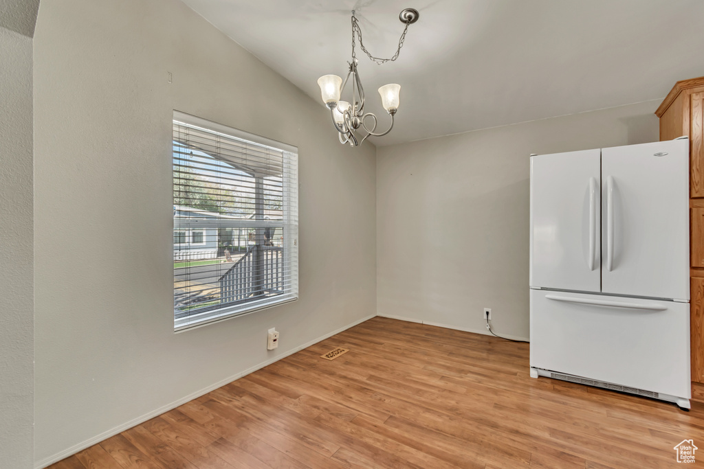 Unfurnished dining area with light wood-type flooring and a notable chandelier