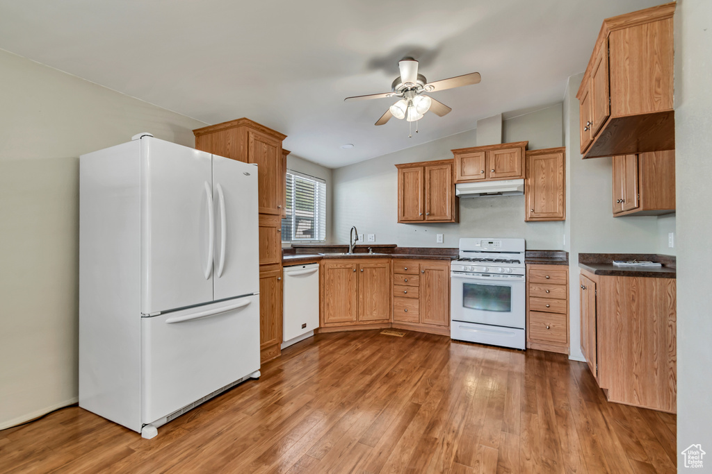Kitchen with dark countertops, ceiling fan, white appliances, and light wood-style flooring