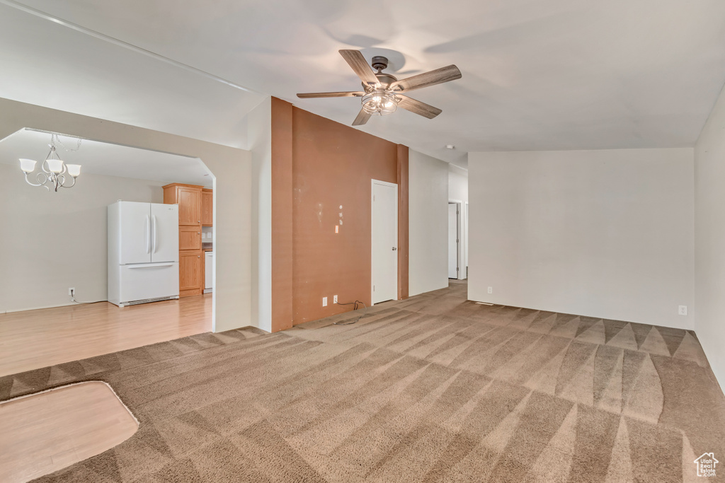 Unfurnished living room with light colored carpet and ceiling fan with notable chandelier