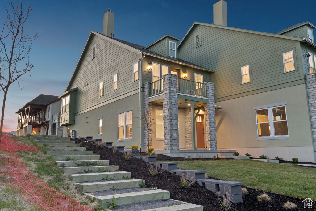 View of front facade with a lawn, a chimney, stucco siding, and a balcony
